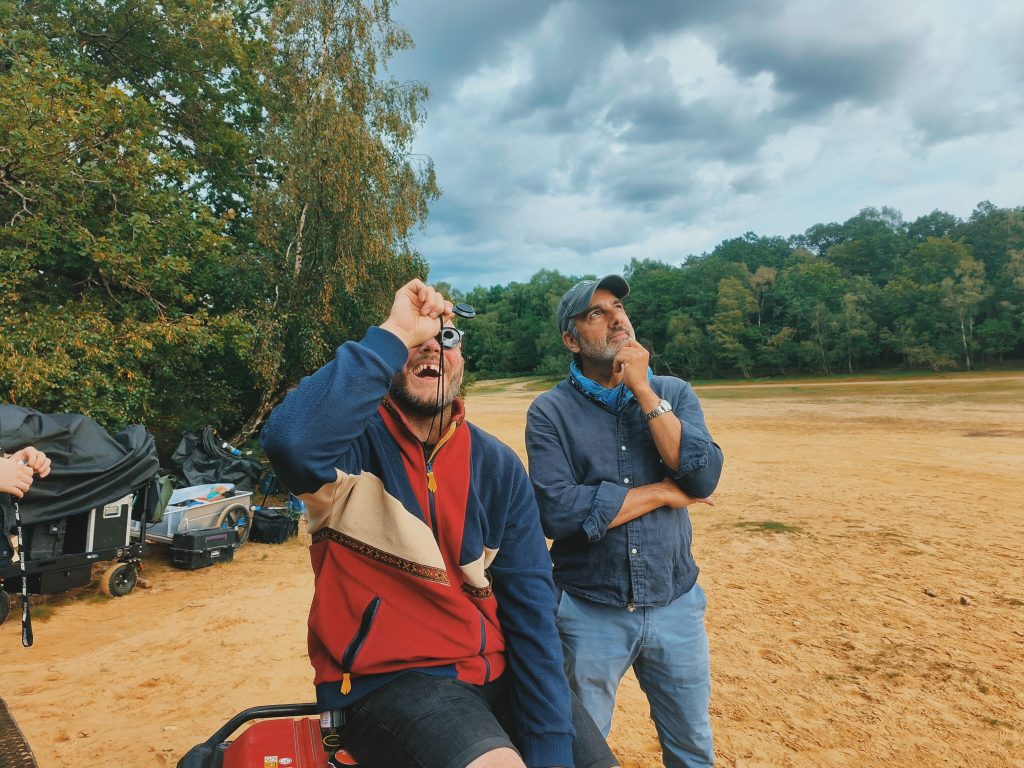 Two men. one sat and one standing looking upwards towards the sky.